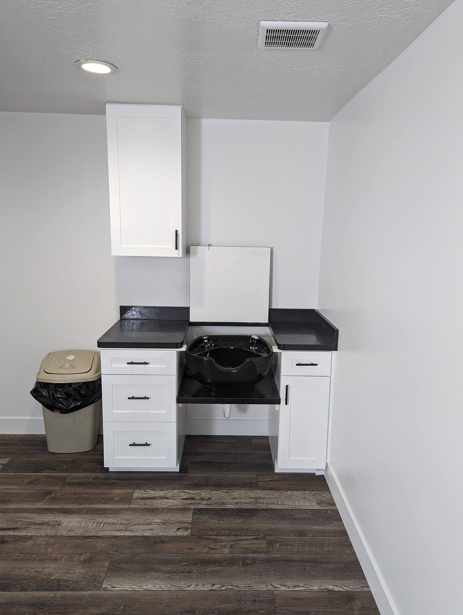 A bathroom with a sink , cabinets , trash cans and a mirror.
