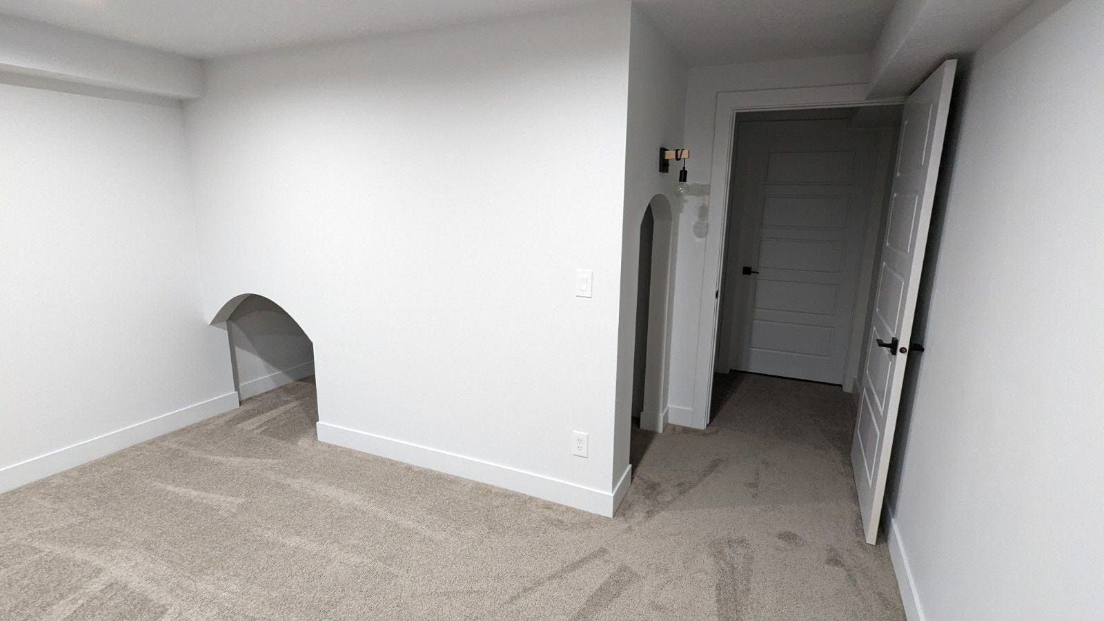 An empty room with a carpeted floor , white walls and a door.