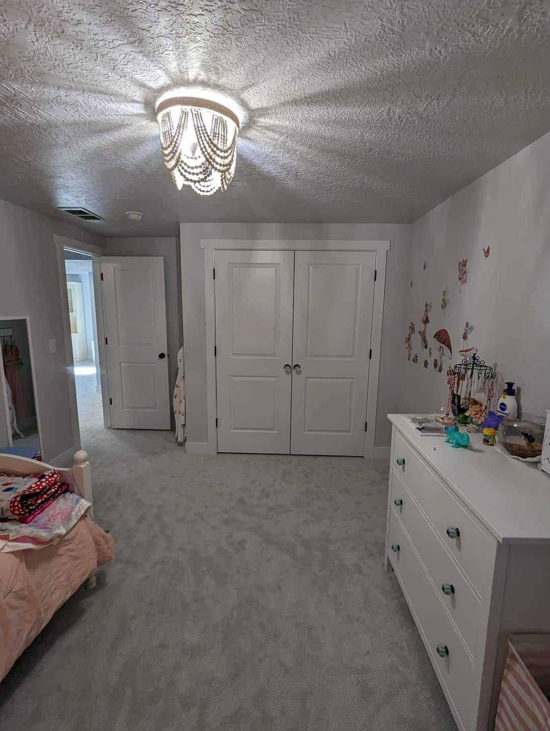 A bedroom with a bed , dresser , and chandelier.