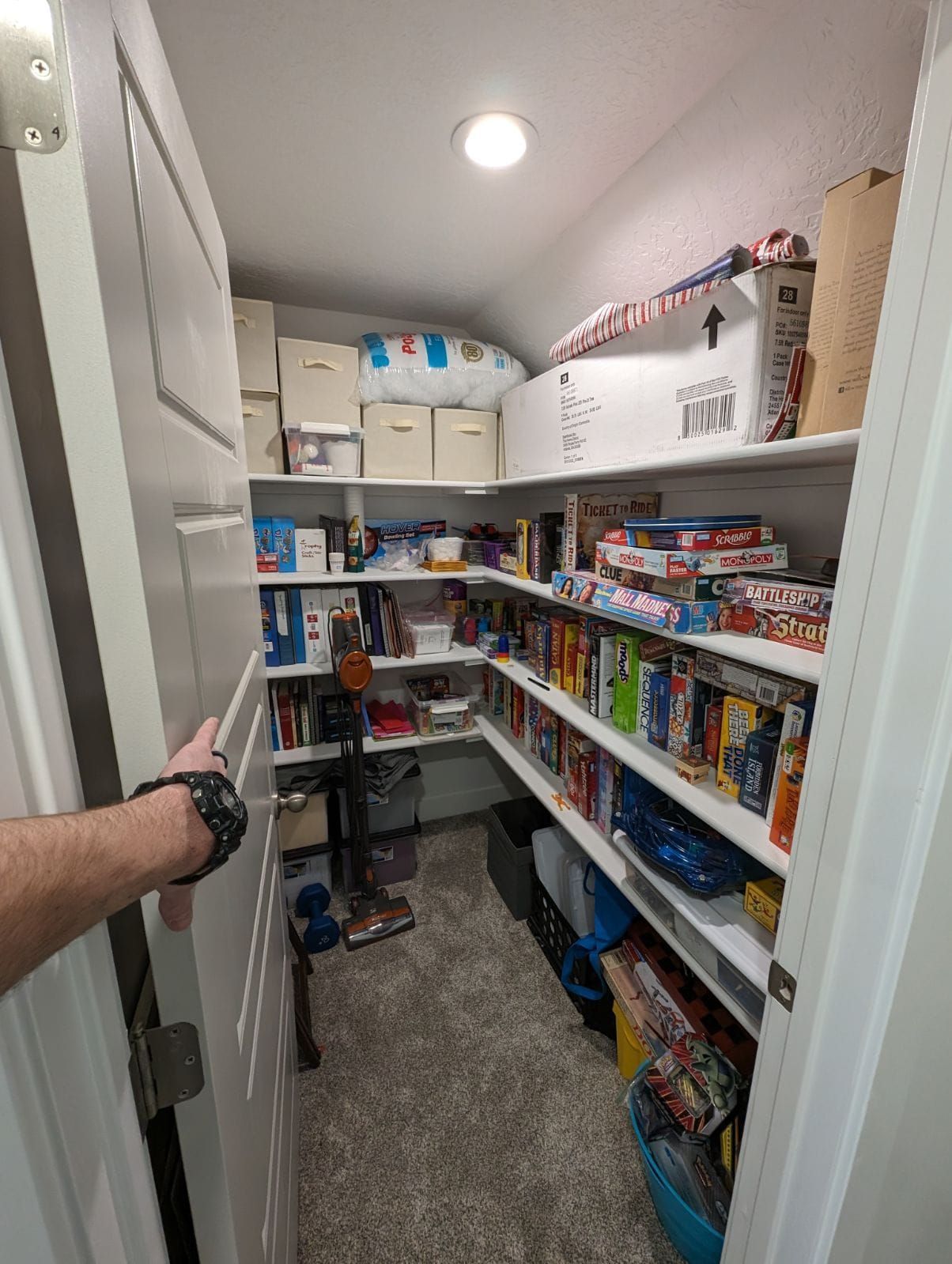 A person is opening a door to a closet filled with lots of toys.