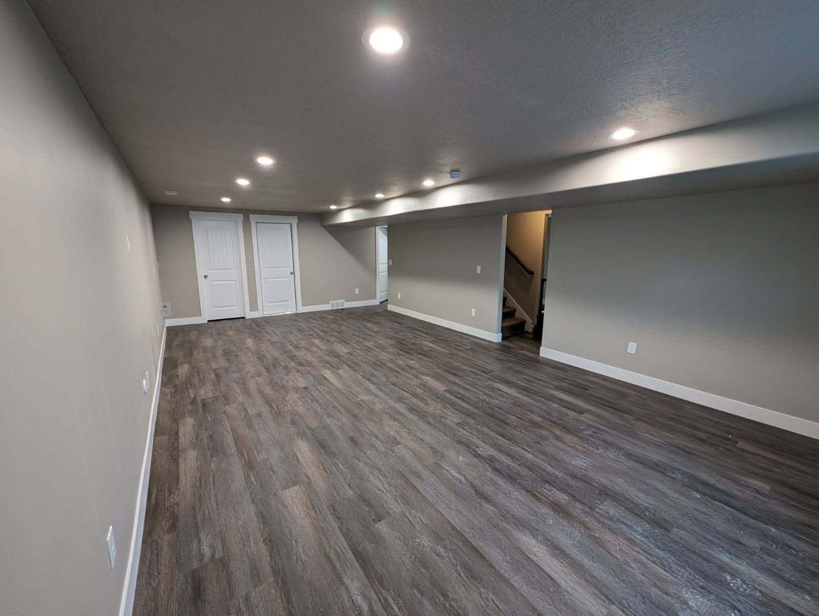 An empty basement with hardwood floors and a staircase.
