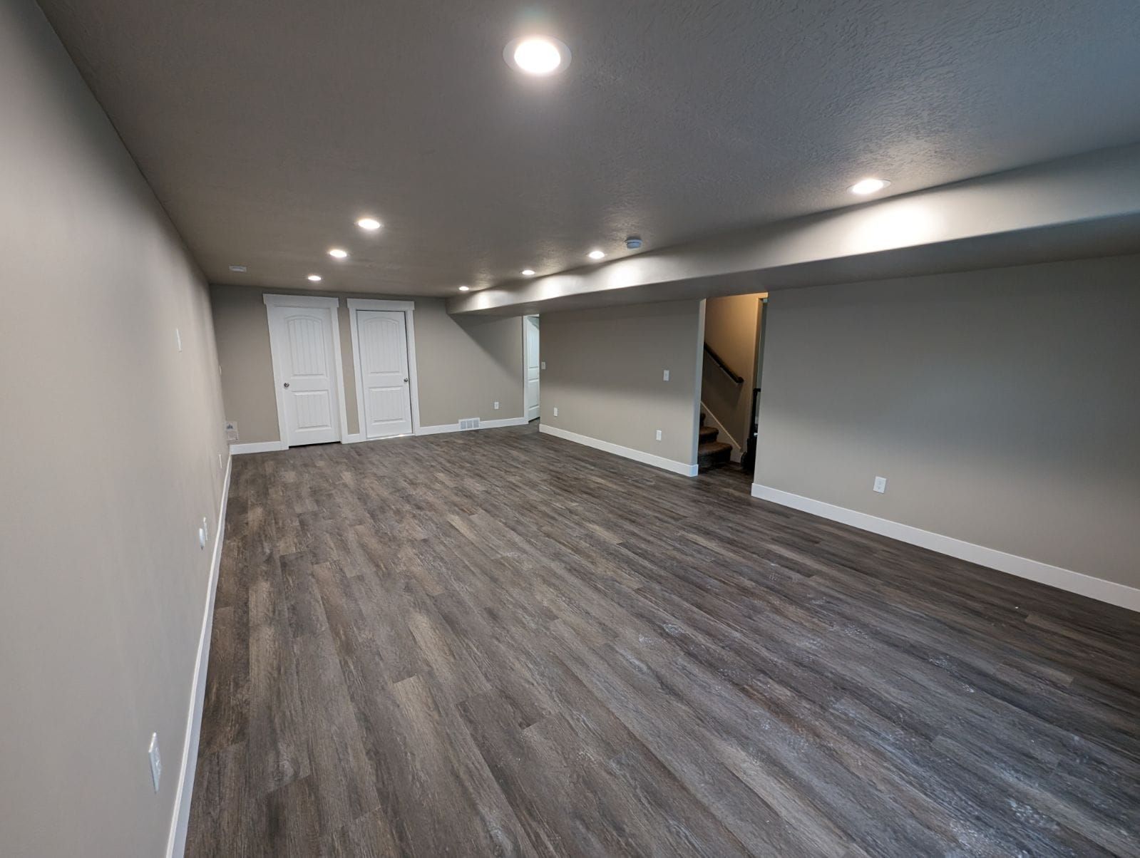 An empty basement with hardwood floors and a staircase.