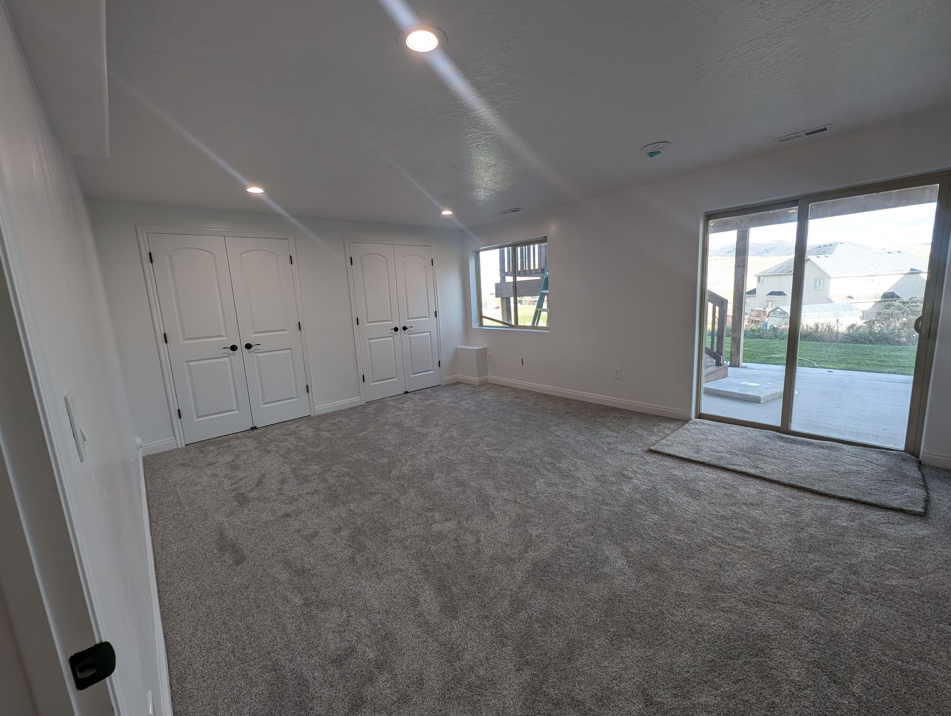 A large empty room with a carpeted floor and sliding glass doors.