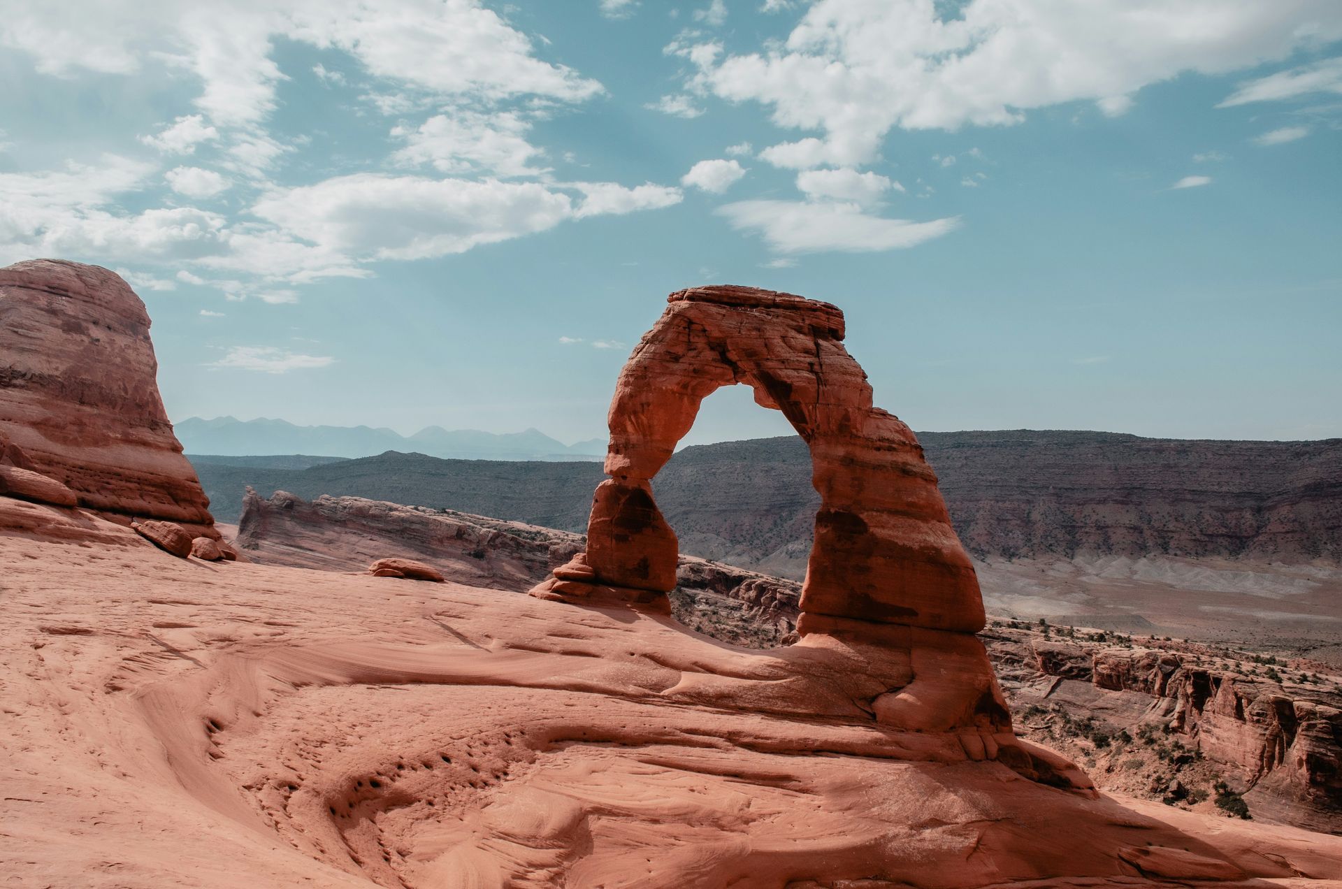 Delicate Arch in Arches National Park, Utah against a rugged desert landscape and partly cloudy sky