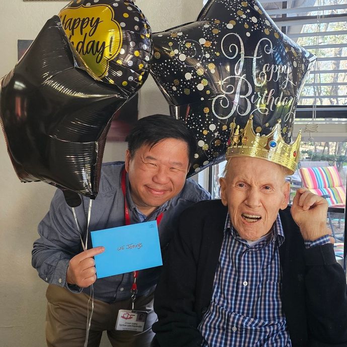 A man holds a birthday card next to an elderly person wearing a gold crown, flanked by 
