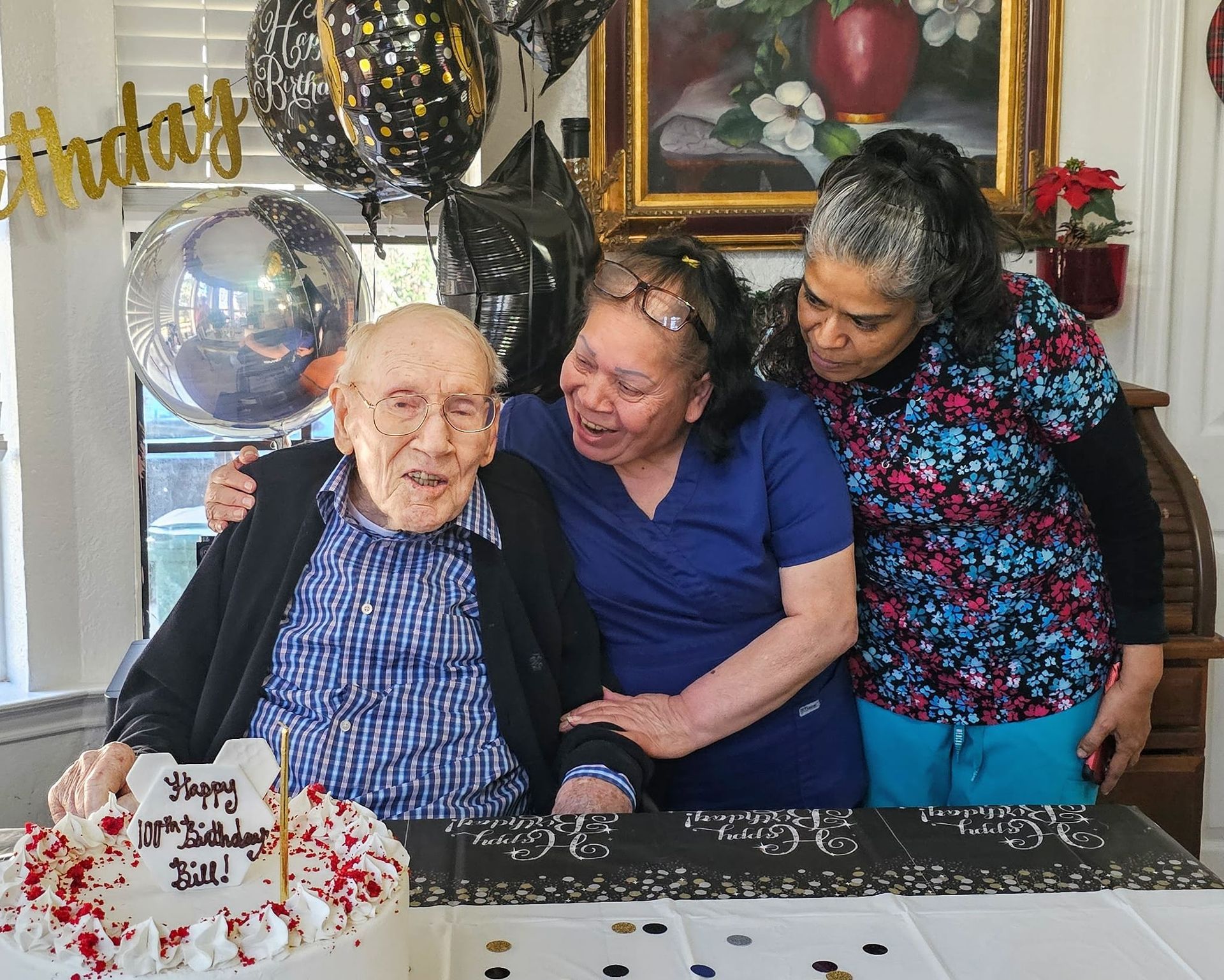 A person celebrating their 107th birthday with a cake and two companions in a decorated room.
