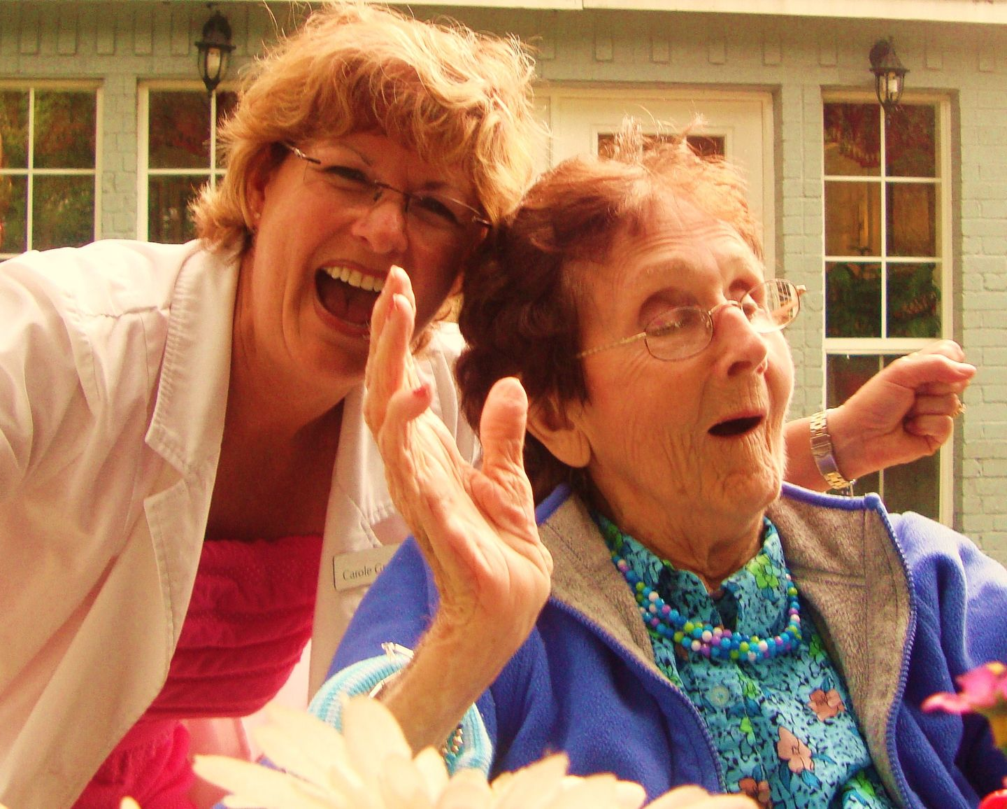 Two people laughing and gesturing with excitement outdoors in front of a building with windows.