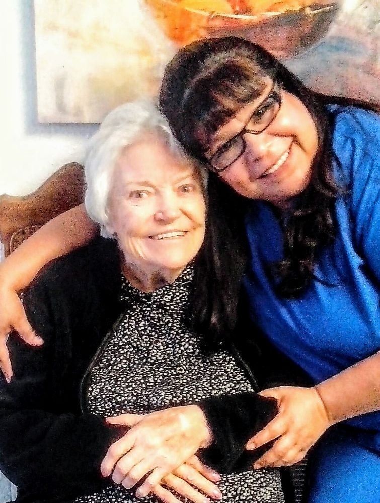 Two smiling people embrace, one wearing a black patterned top and the other wearing a blue shirt.