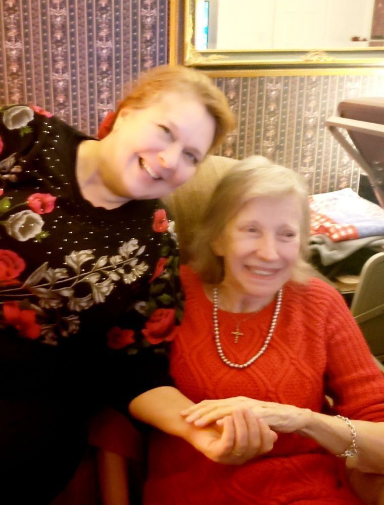 Two people smiling while holding hands, with one in a floral black sweater and the other in a red sweater.