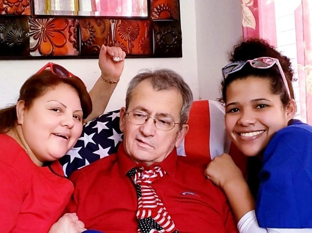 Three people smiling together: a person in red on the left, an older person in a red shirt with a patterned tie, and a person in a blue shirt on the right.