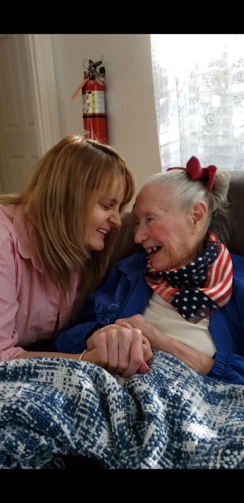 Two people holding hands and smiling at each other, one wearing a patriotic scarf and red hair bow, under a blue blanket.
