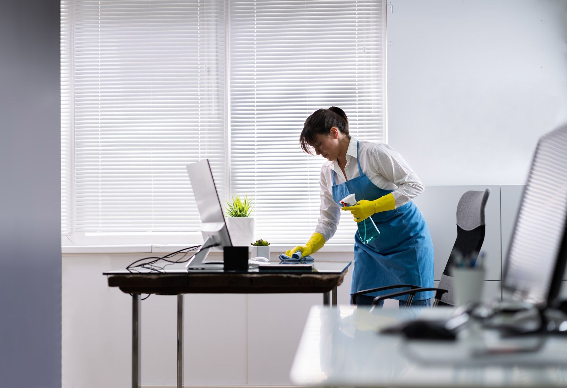 A woman is cleaning a desk in an office with a computer.