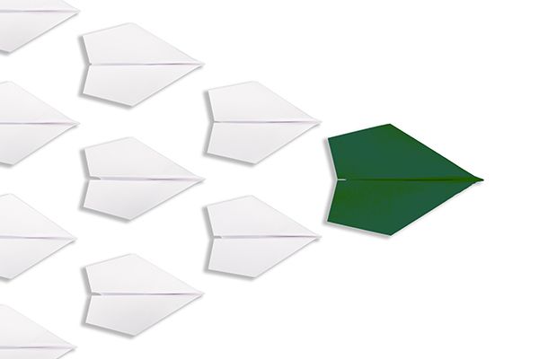 A green paper airplane is leading a group of white paper airplanes.