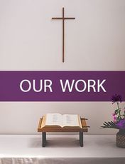 There is a cross on the wall above a bible on a table.