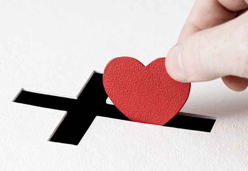 A person is putting a red heart into a black cross
