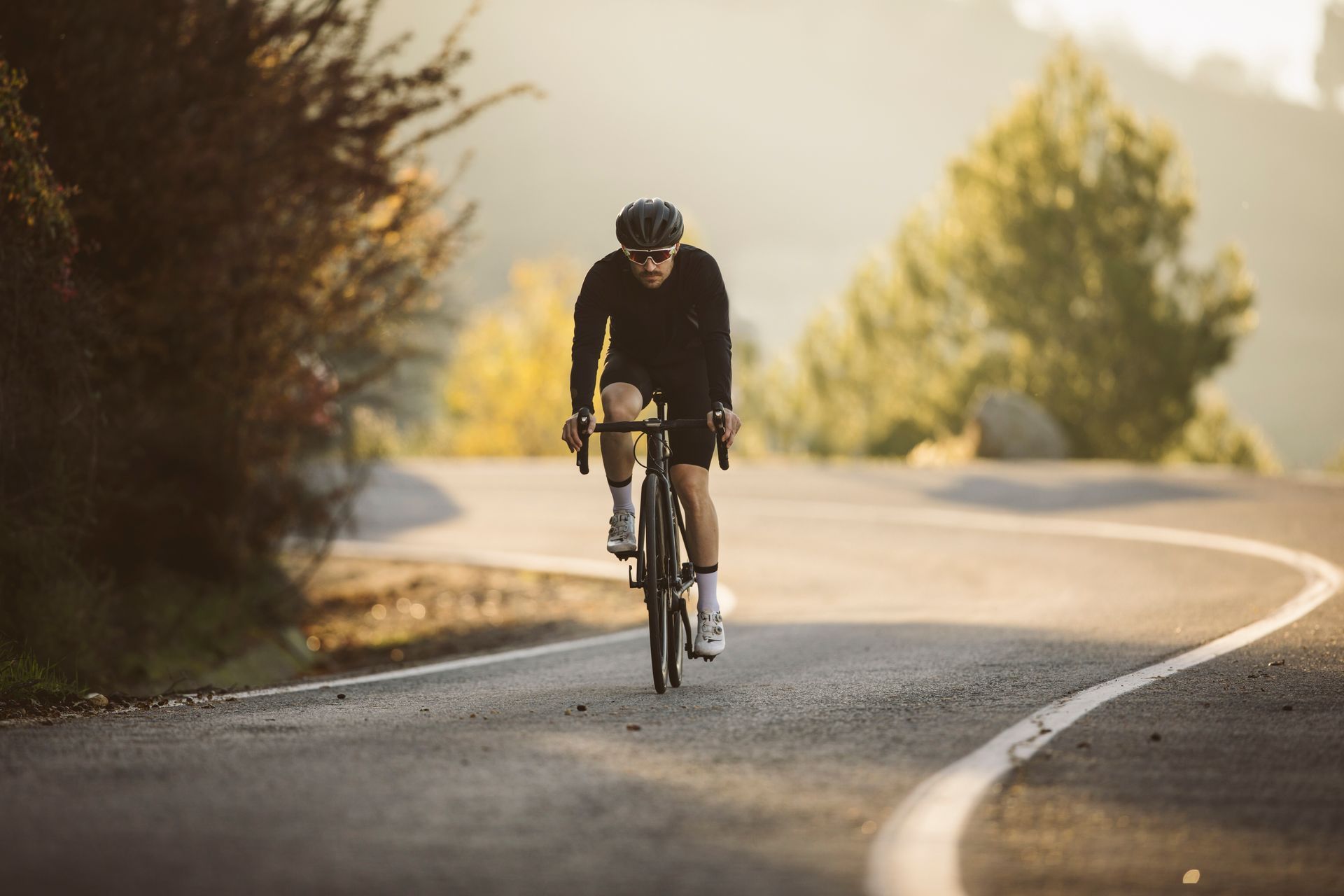 A cyclist rides a road bike down a curving paved path bathed in warm, golden sunlight.