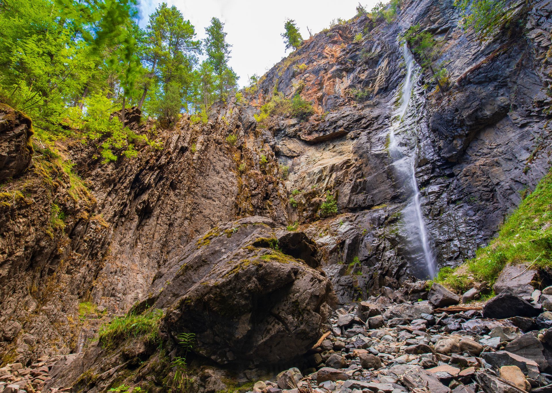 Waterfall cascading down a rocky cliff with green trees and boulders below