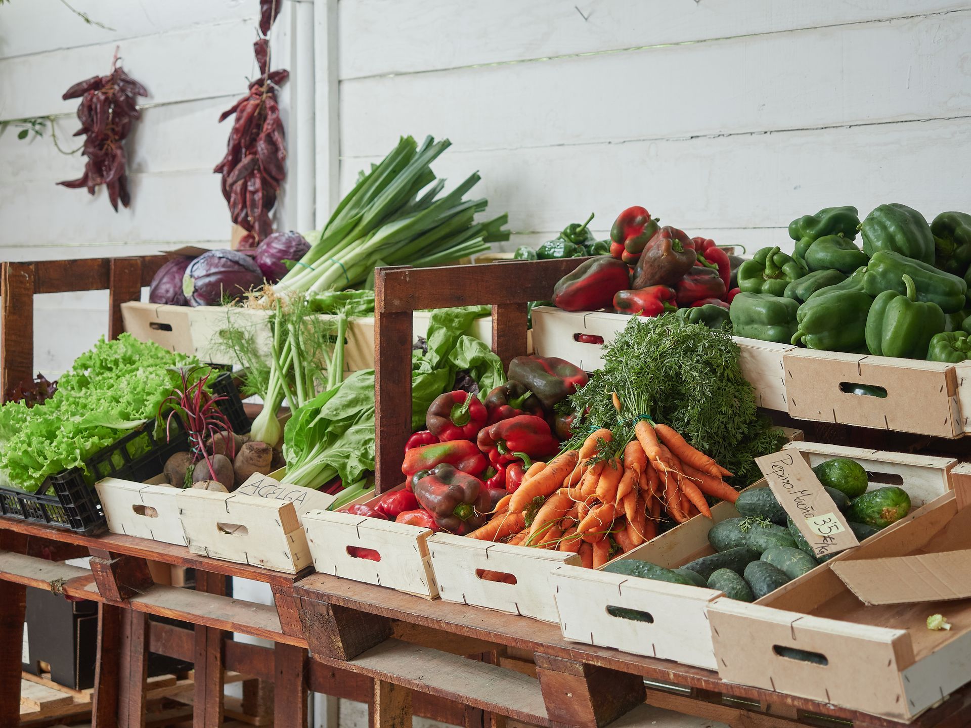 Assorted fresh vegetables and herbs displayed in wooden crates at an outdoor market stall