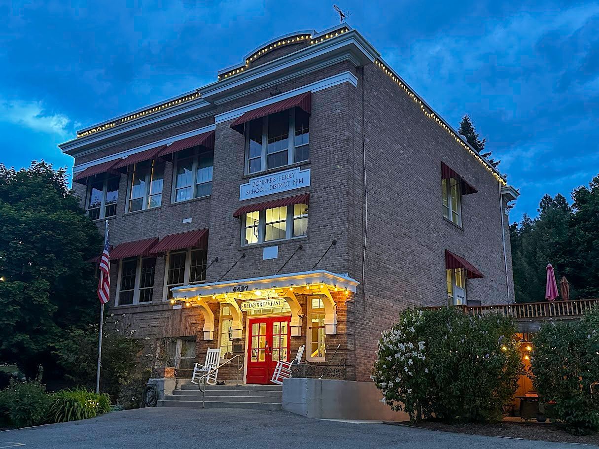 Illuminated brick building at dusk with a red entrance and blue evening sky