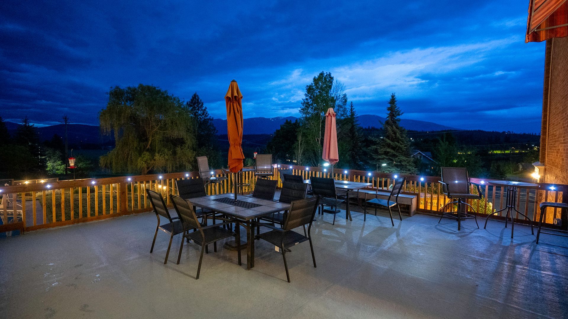 Outdoor patio with tables and umbrellas at dusk, overlooking trees under a blue evening sky