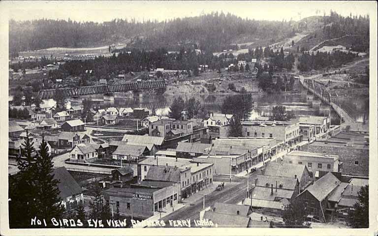 A black-and-white vintage bird's-eye view of Bonners Ferry, Idaho, showing a small town nestled in a forested valley.