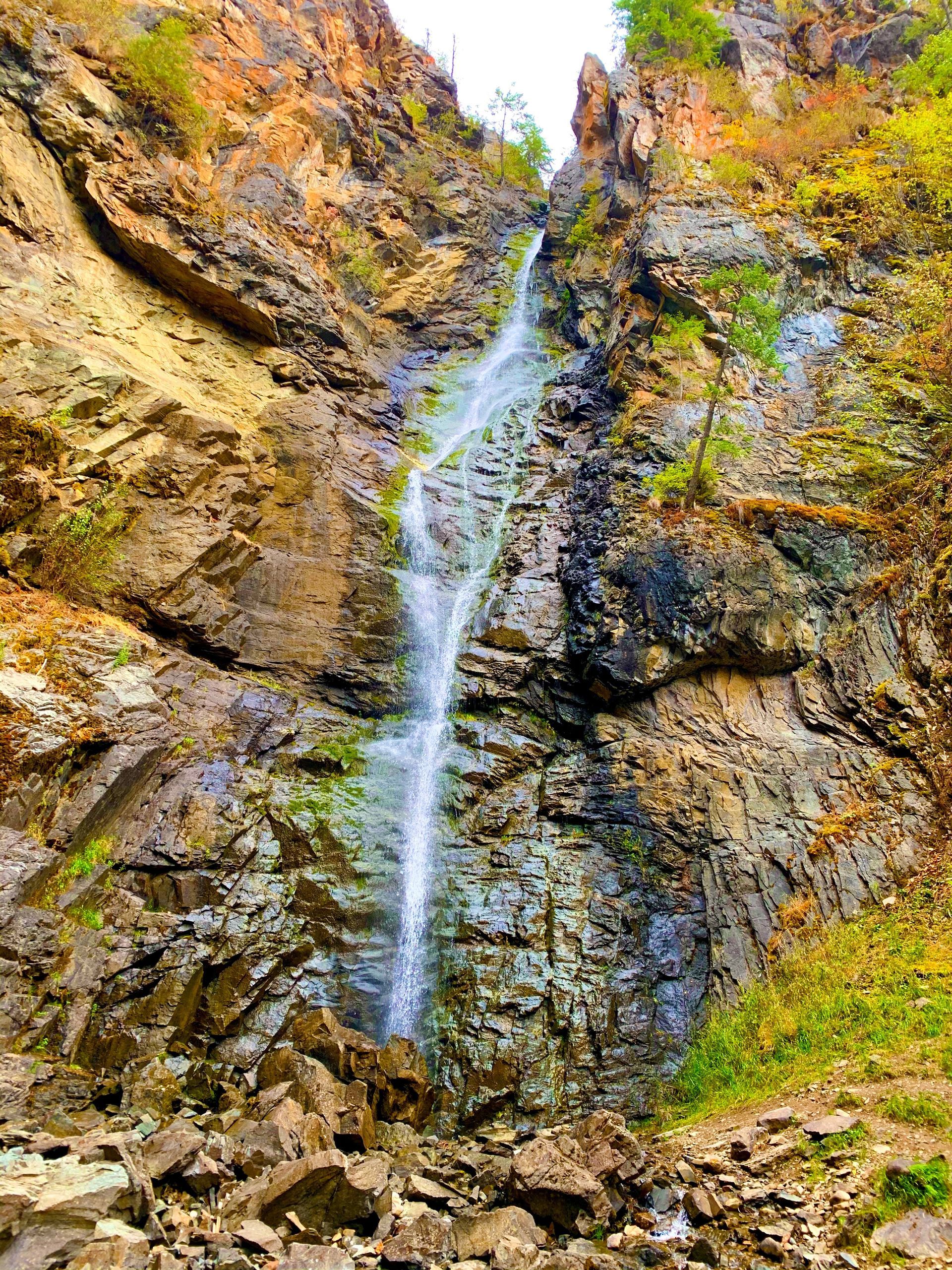 A slender waterfall flows down a steep, rocky cliffside surrounded by autumn-colored foliage.