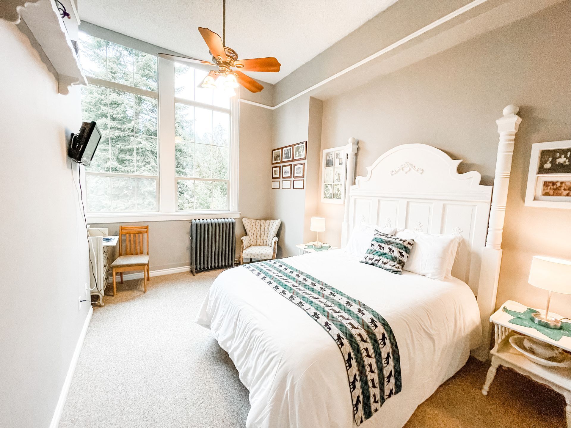 A bright, cozy bedroom featuring a white four-poster bed with a patterned runner, a wooden chair, and large windows.