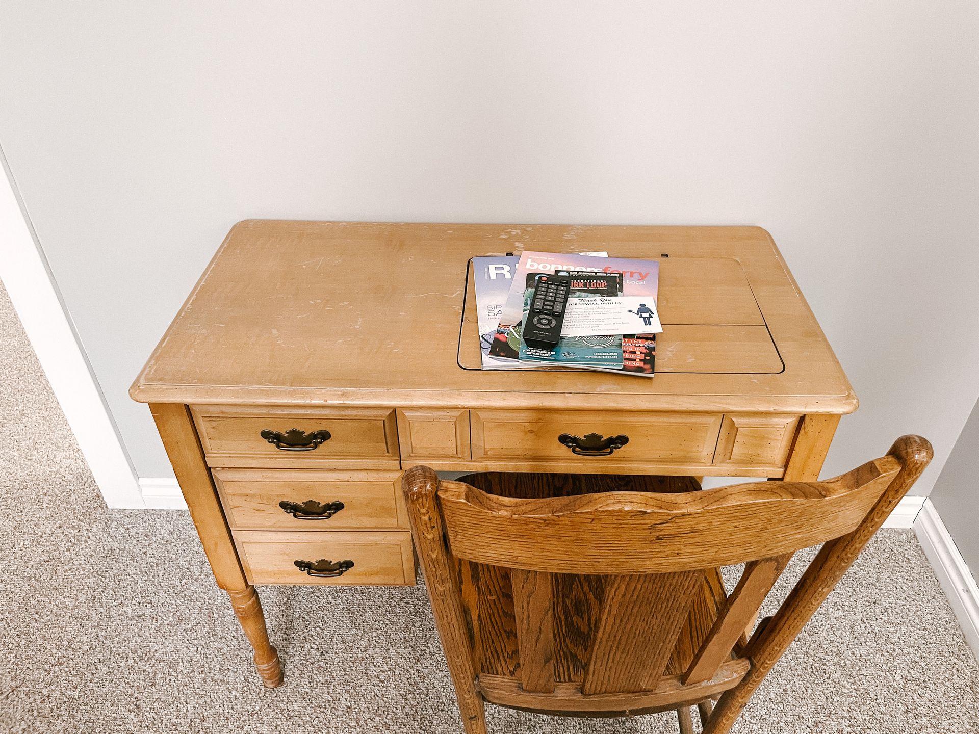 A wooden desk with three drawers and a matching wooden chair, with a small black object resting on the desktop.