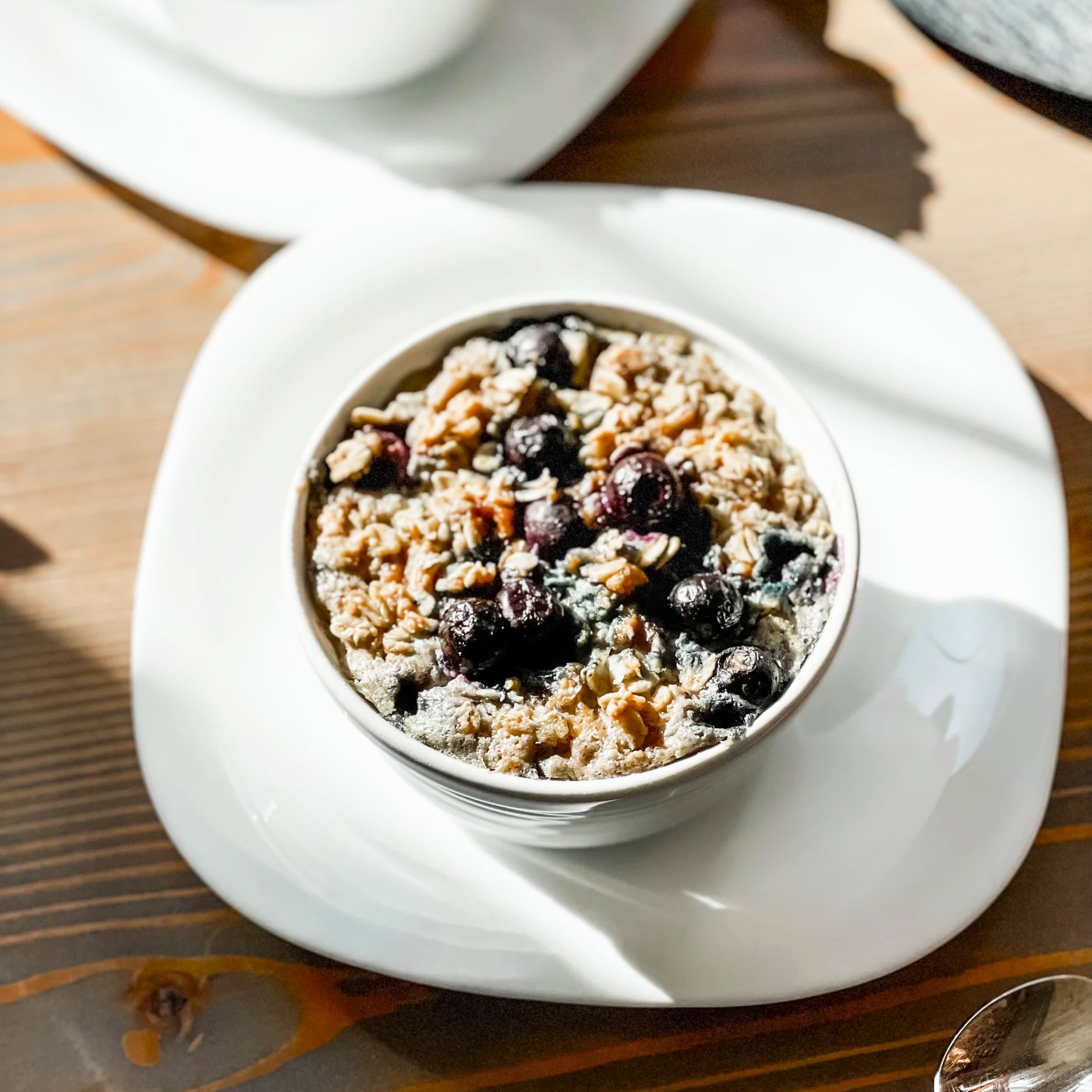 A single bowl of oatmeal topped with blueberries, served on a white plate on a wooden table.