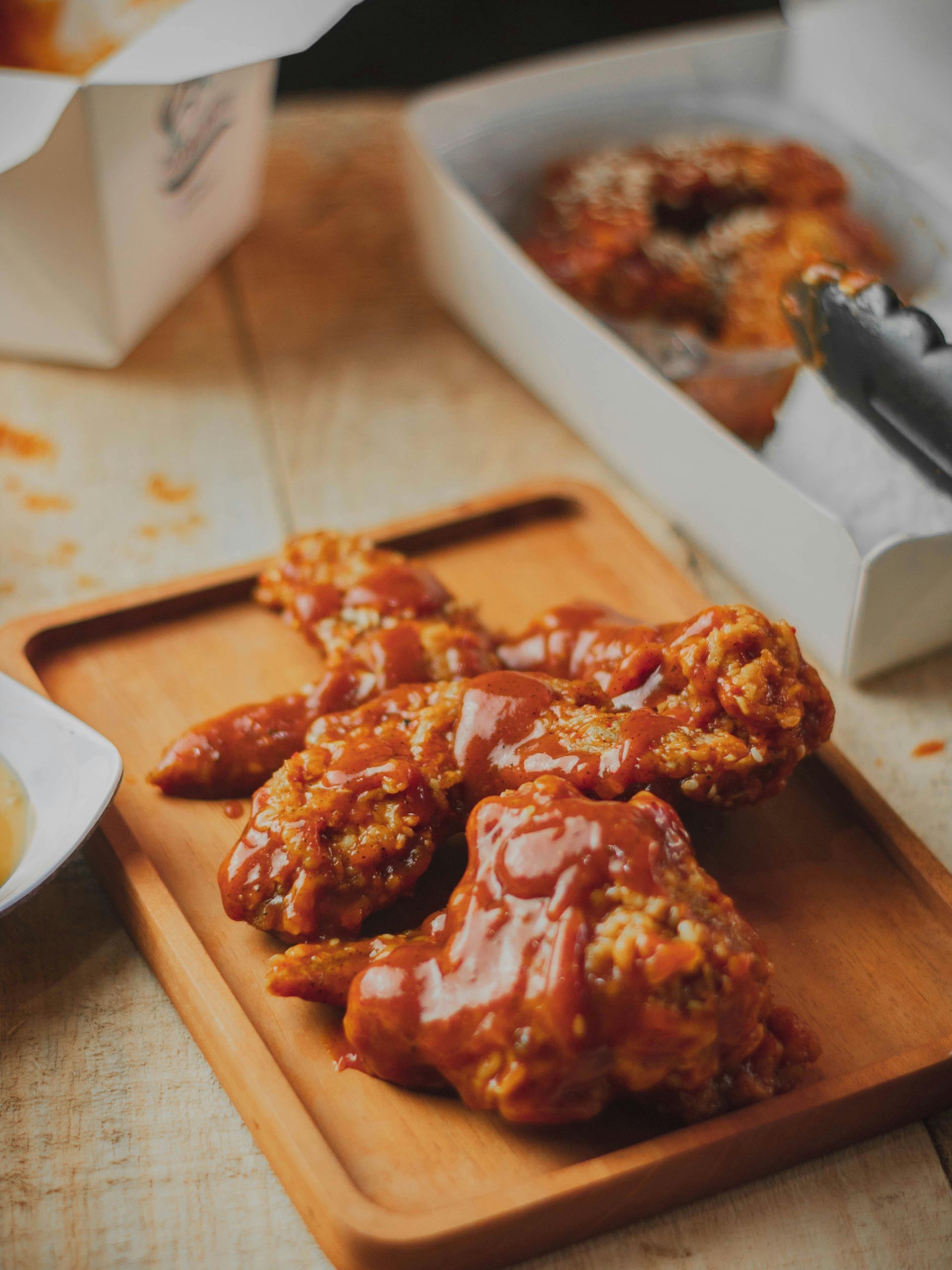 A wooden tray holds several golden-brown fried chicken wings generously coated in a thick, reddish-brown barbecue sauce.