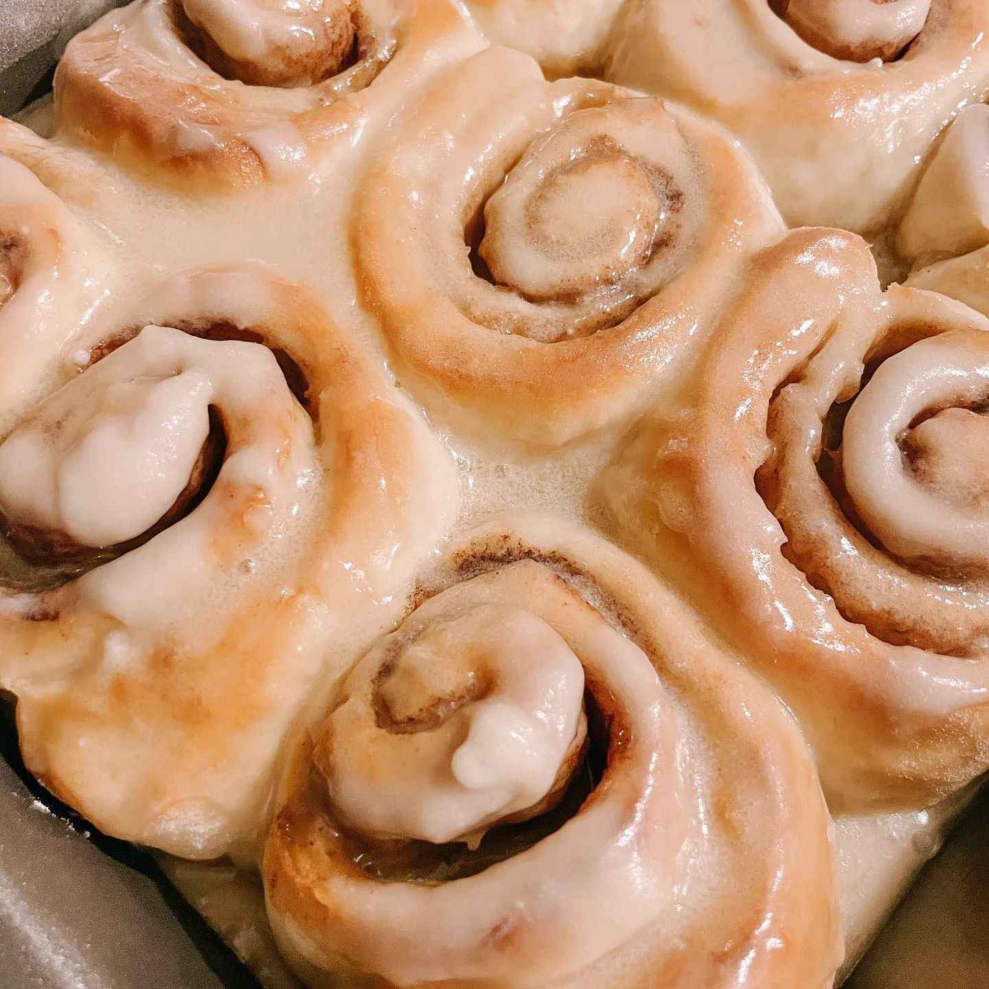 A close-up of golden-brown cinnamon rolls topped with a thick, glossy white glaze in a baking pan.