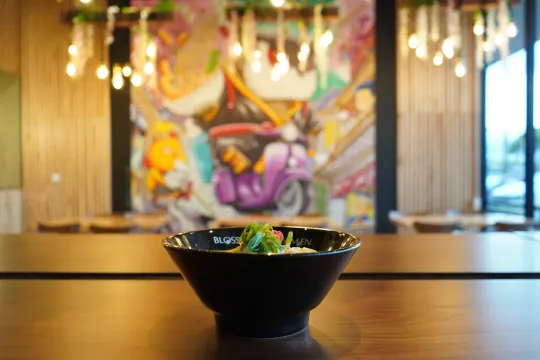 Black bowl of food on a wooden table, with a colorful mural softly blurred in the background