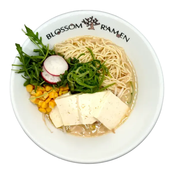 White ramen bowl with noodles, tofu, corn, greens, radish, and chives.