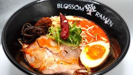 Bowl of ramen with sliced pork, soft-boiled egg, seaweed, and green onions in a black bowl