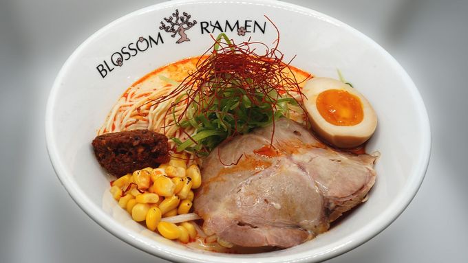 Bowl of ramen with sliced pork, soft-boiled egg, corn, greens, and spicy chili topping