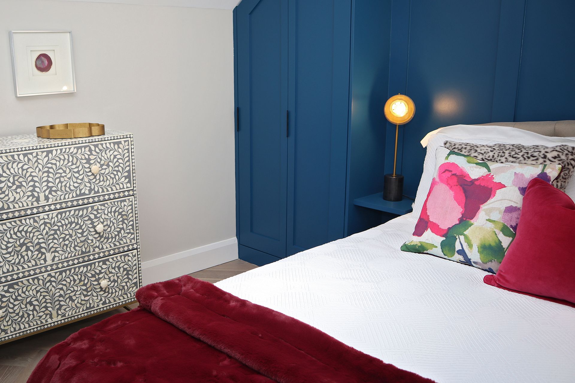 A bedroom with a bed , dresser , and lamp.