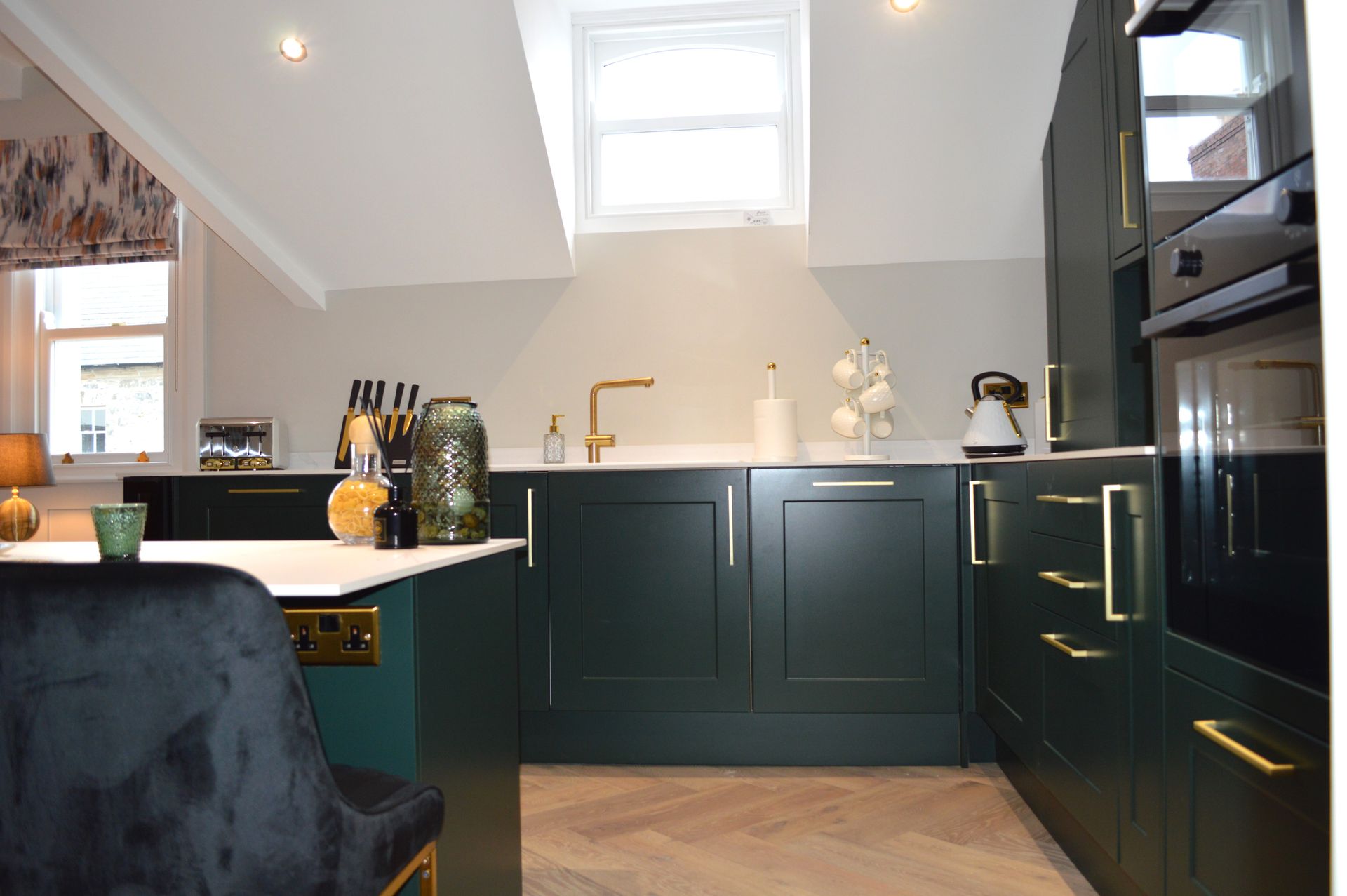 A kitchen with green cabinets and gold handles and a window.