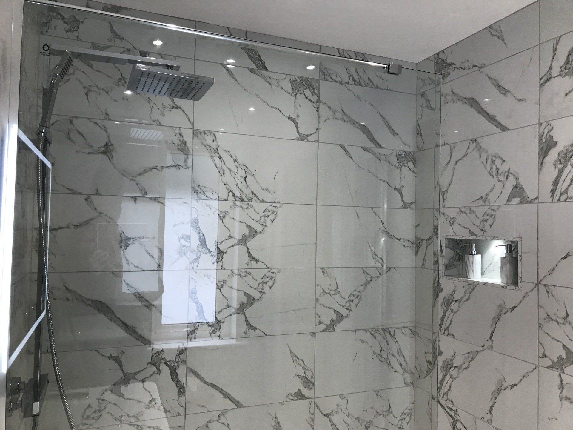 A bathroom with marble tiles and a walk in shower with a glass door.