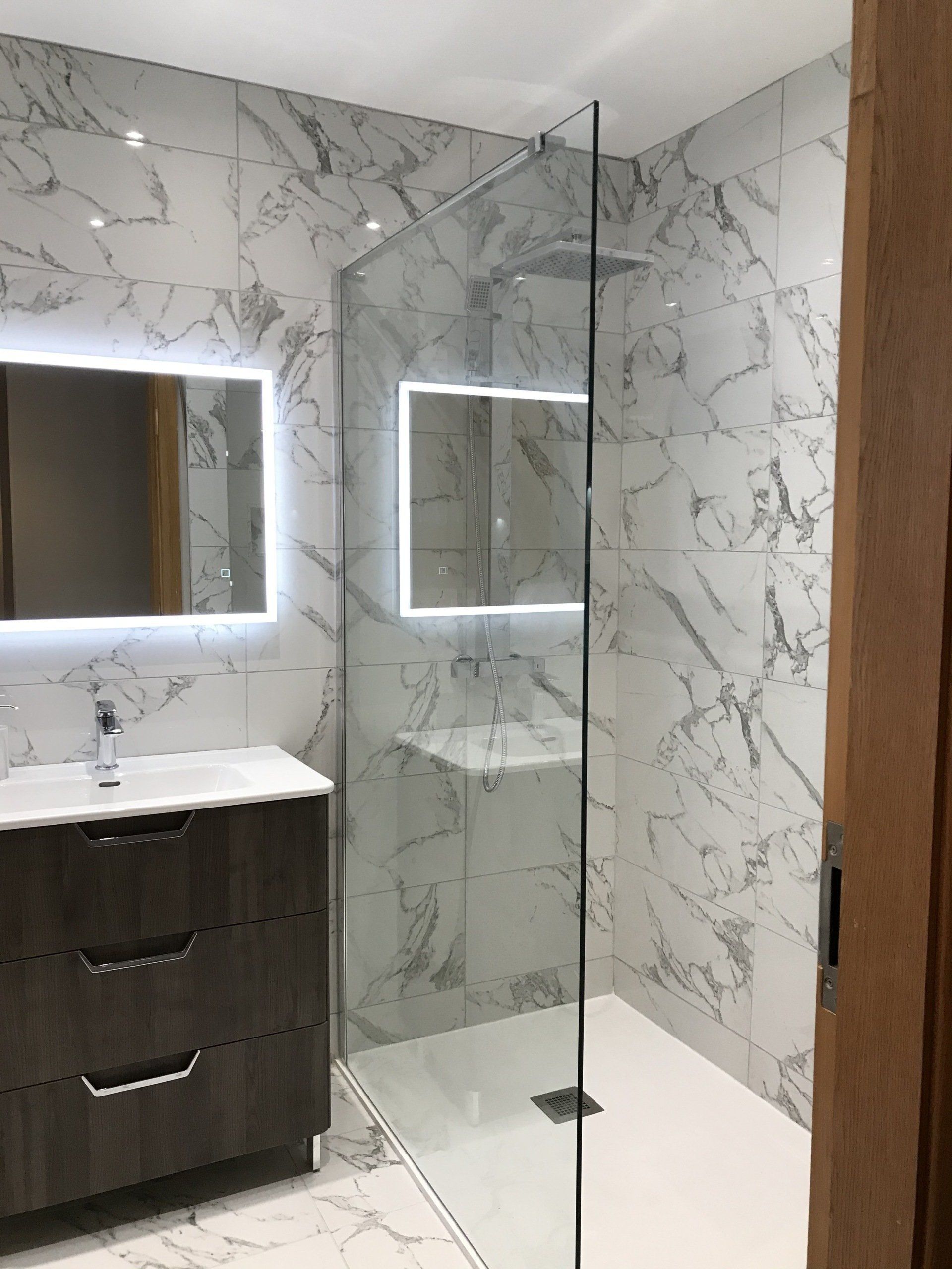 A bathroom with a walk in shower , sink and mirror.