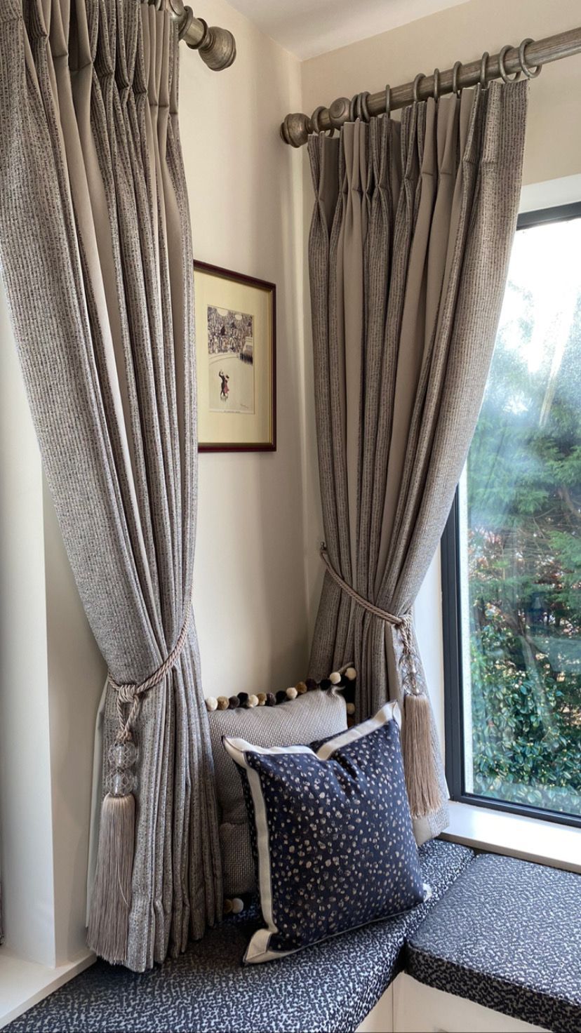 There is a window seat in the corner of the room with curtains and pillows.