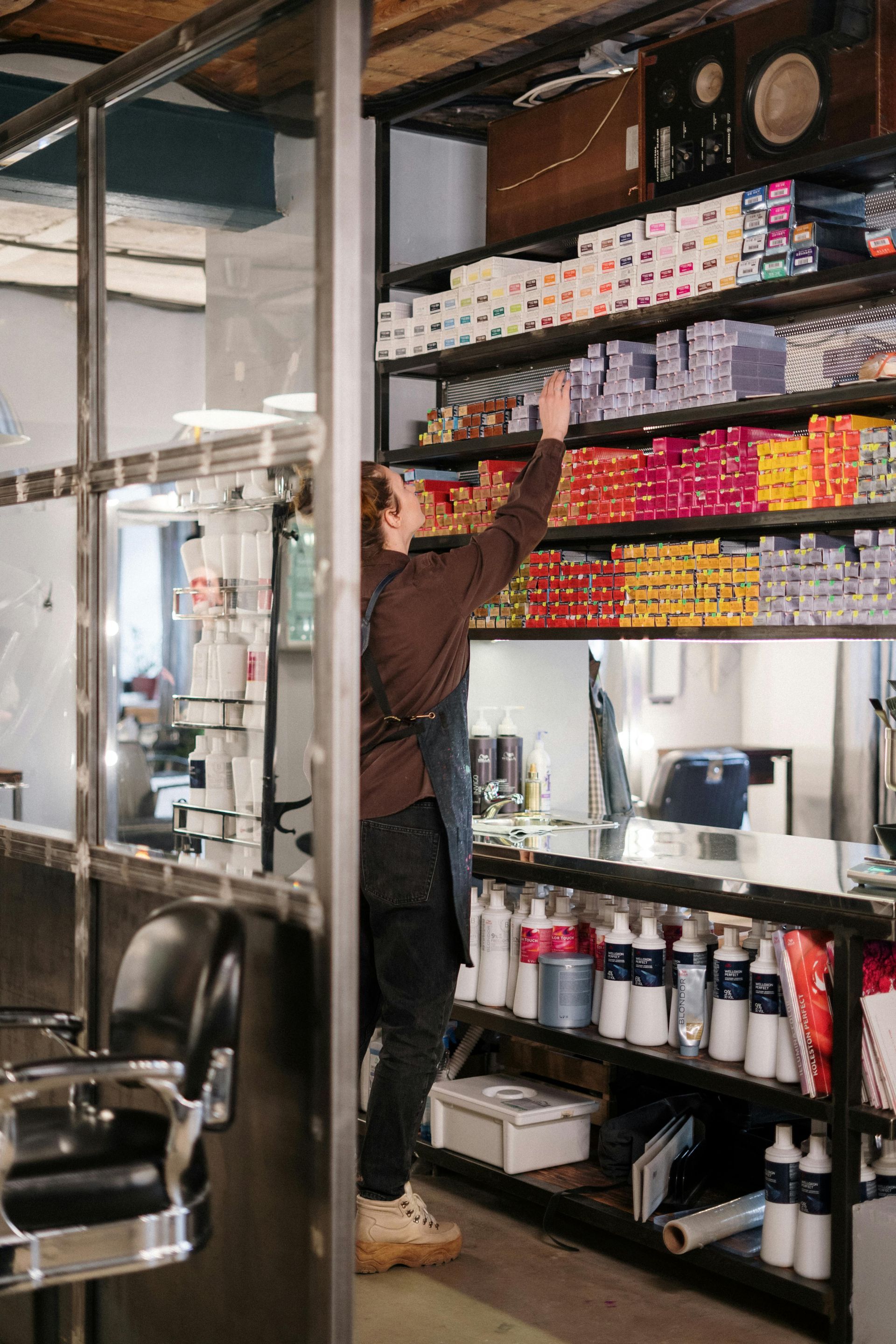 Person reaching for hair dye boxes on a shelf in a salon.