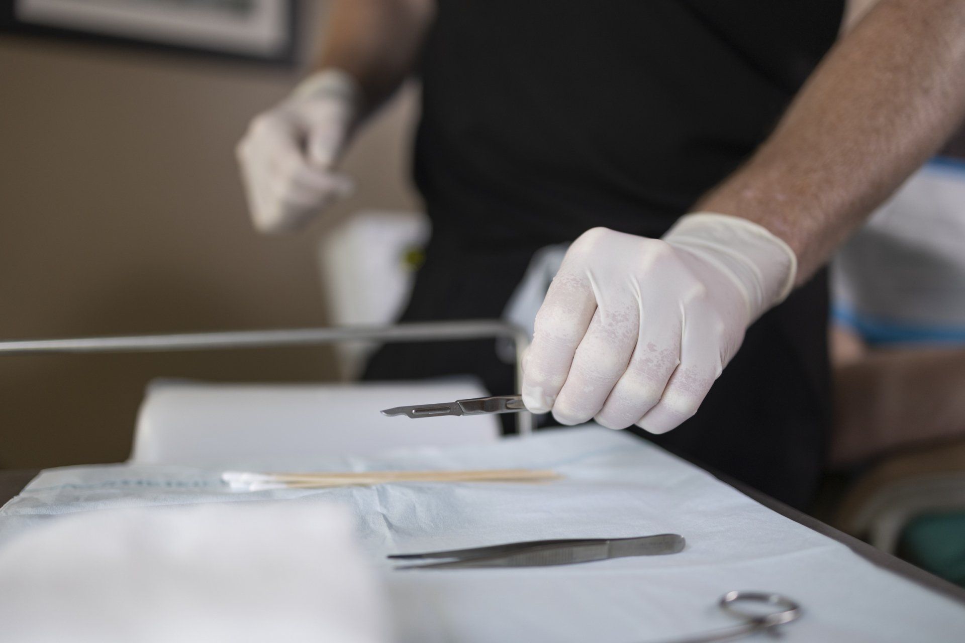 A medical professional in gloves holds a scalpel above a sterile tray with surgical tools.