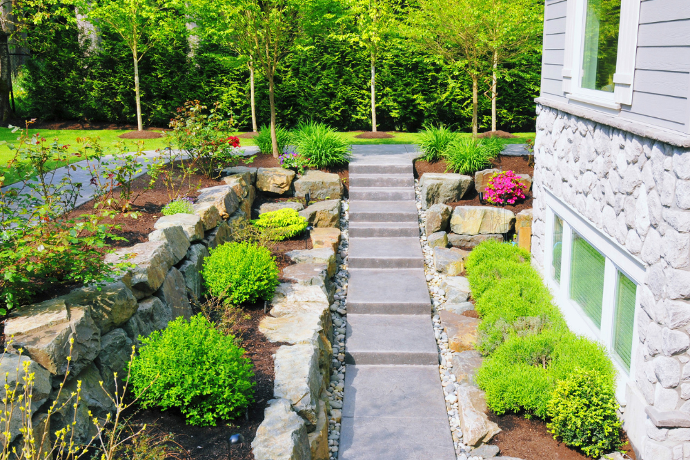 A stone walkway leading to a house surrounded by trees and bushes.