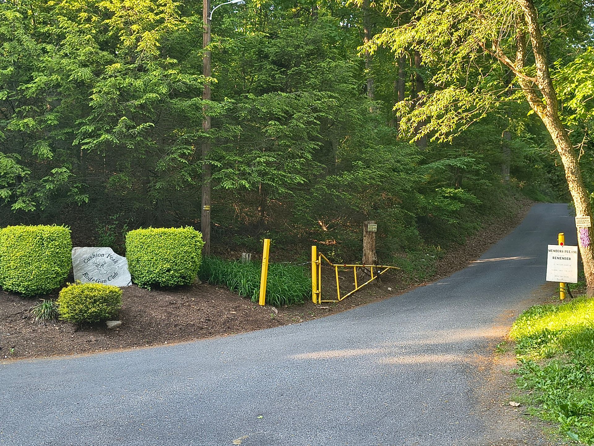 Gravel driveway curving into a wooded area with yellow posts and a small sign at the entrance