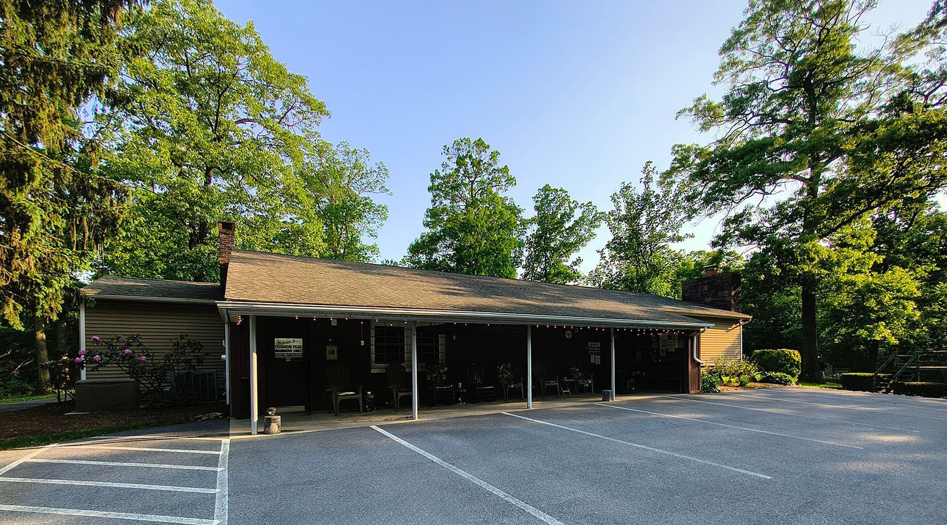 Small roadside building with a covered porch, surrounded by trees and an empty gravel lot