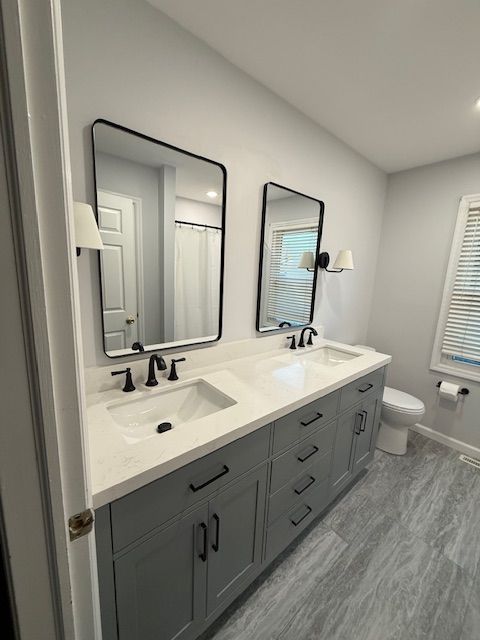A bathroom remodel by Reliable General Contracting in Collegeville with two sinks , two mirrors and a toilet.