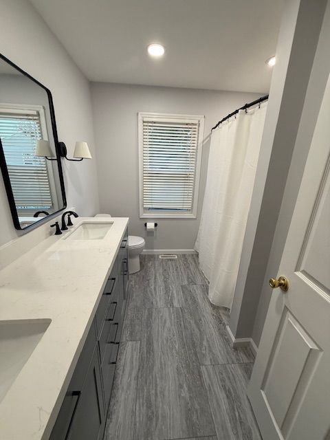 A bathroom remodel by reliable general contracting with two sinks , a toilet , and a shower curtain.
