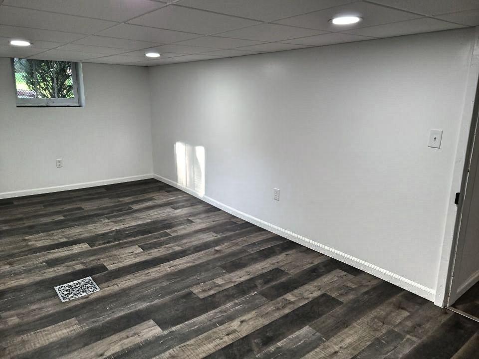 An empty basement with hardwood floors and white walls.