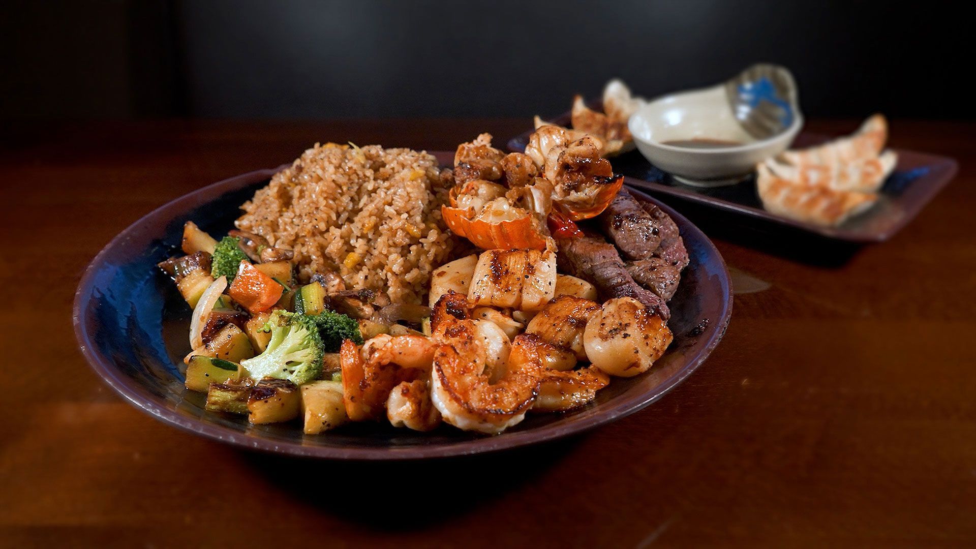 A plate of food with shrimp , rice and vegetables on a wooden table.