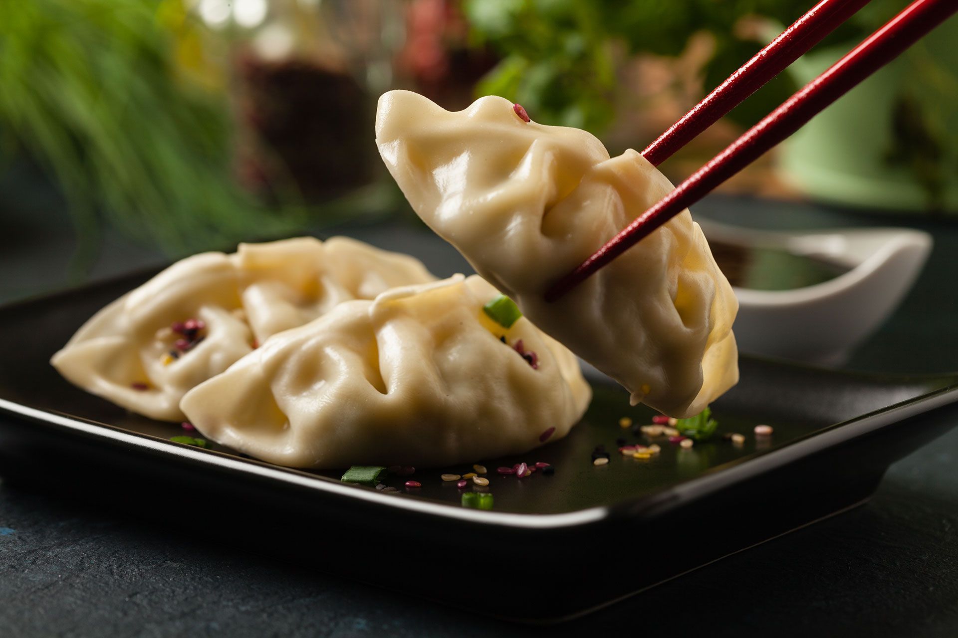A person is eating a dumpling with chopsticks on a black plate.